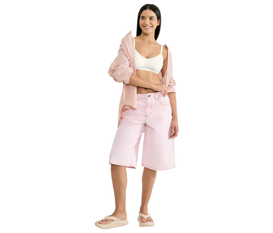 Frau trägt ein weißes Bralette, eine rosa gestreifte Hemdbluse und rosa Culottes mit beigen Flip-Flops.