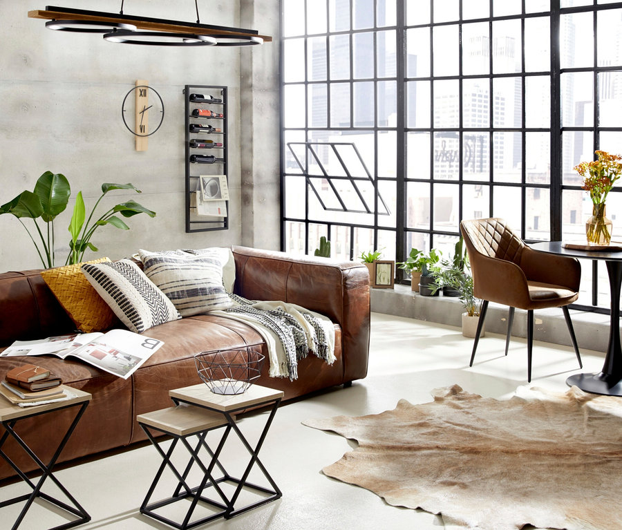 Wohnzimmer mit braunem Ledersofa, Couchtisch, Stuhl und großem Fenster.