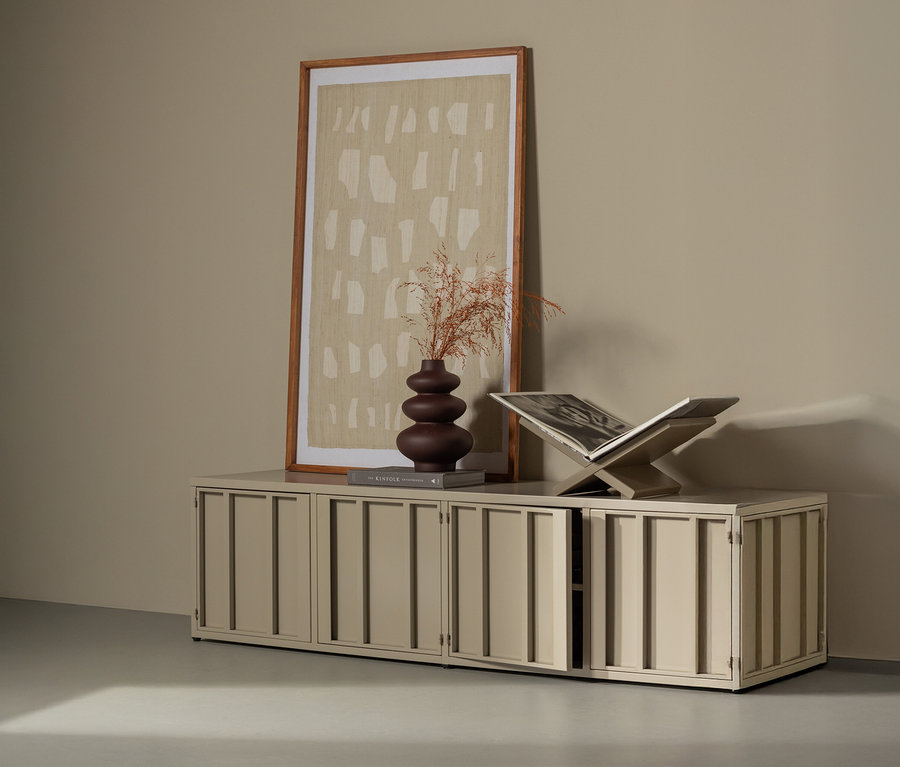 Ein sandfarbener WOOOD Metall-TV-Schrank »Level« steht vor einer Wand mit einem gerahmten Bild. Auf dem Schrank stehen eine braune Vase mit Trockenblumen und ein Buchständer mit einem Buch.