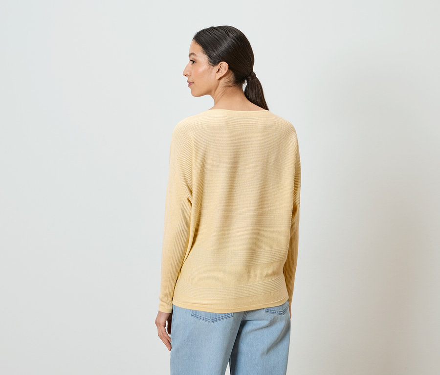 Eine Frau mit Pferdeschwanz trägt einen gelben Pullover und hellblaue Jeans.