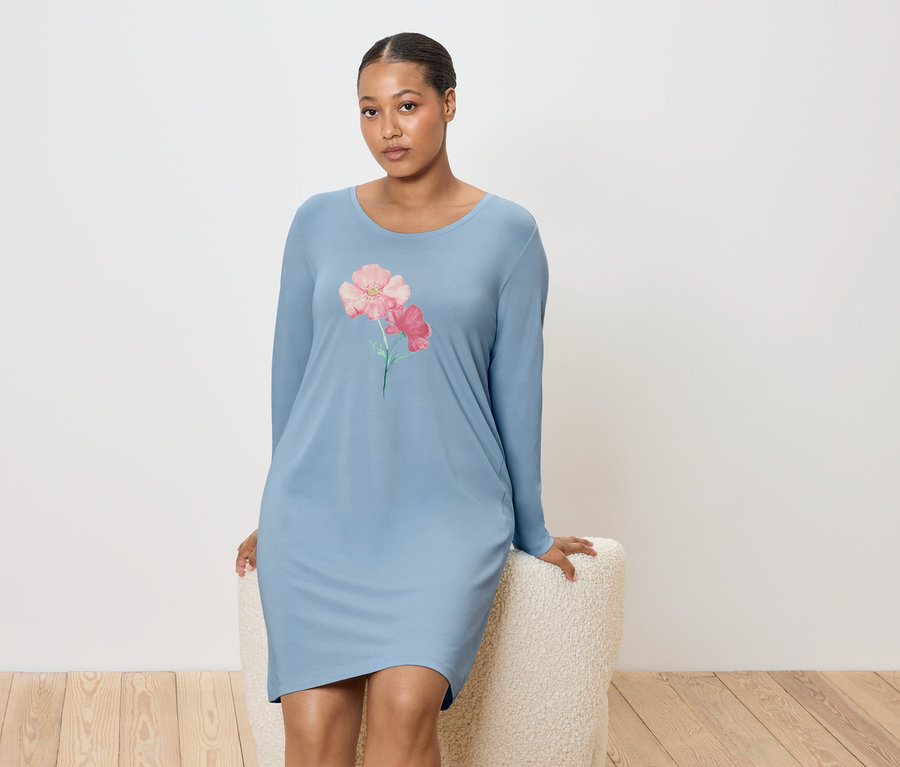 Frau sitzt auf einem Hocker und trägt ein blaues Nachthemd mit Blumenmuster.