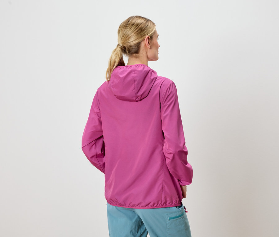 Rückansicht einer Frau mit blonden Haaren, die eine pinkfarbene Jacke mit Kapuze und blaue Hosen trägt.