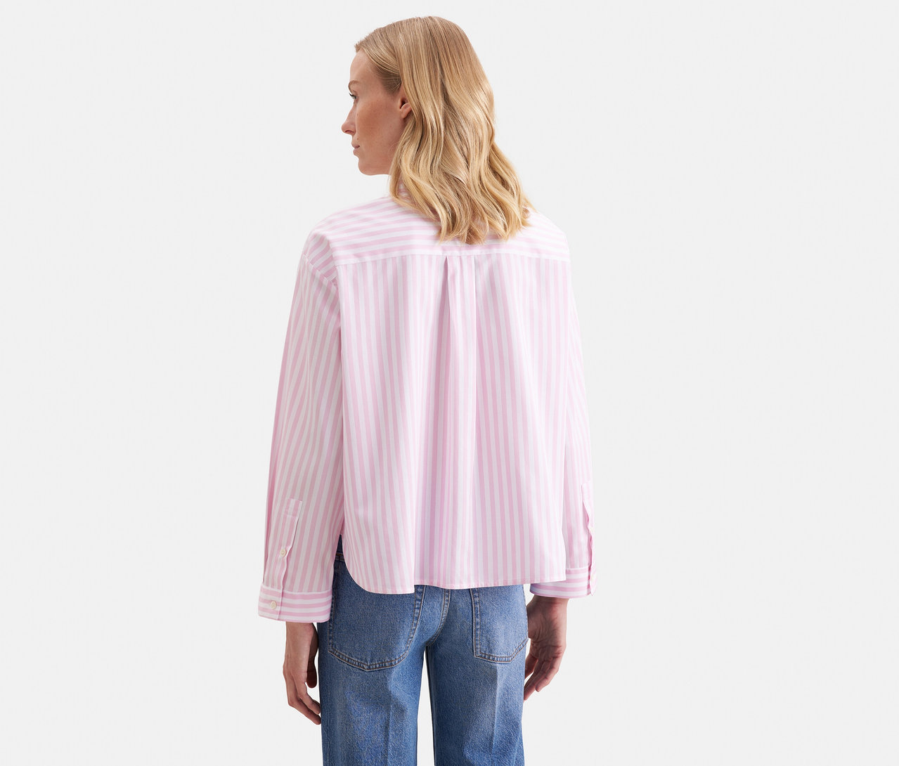 Frau von hinten, trägt eine roséfarbene, gestreifte Seidensticker Oversize Hemdbluse und blaue Jeans.