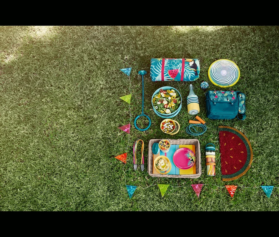 Auf einer Wiese liegen eine Picknickdecke, eine LED-Wurfscheibe, ein Springseil, ein Fahrrad-Spanngurt, ein Korbtablett, eine Kokos-Fußmatte, eine Flaschen-Kühlmanschette, eine Salatschüssel, 4 Picknickteller, eine Fahrradklingel, eine LED-Lichterkette »Wimpel«, eine XL-Picknickdecke, ein LED-Hüpfspiel und eine Mini-Kühltasche.