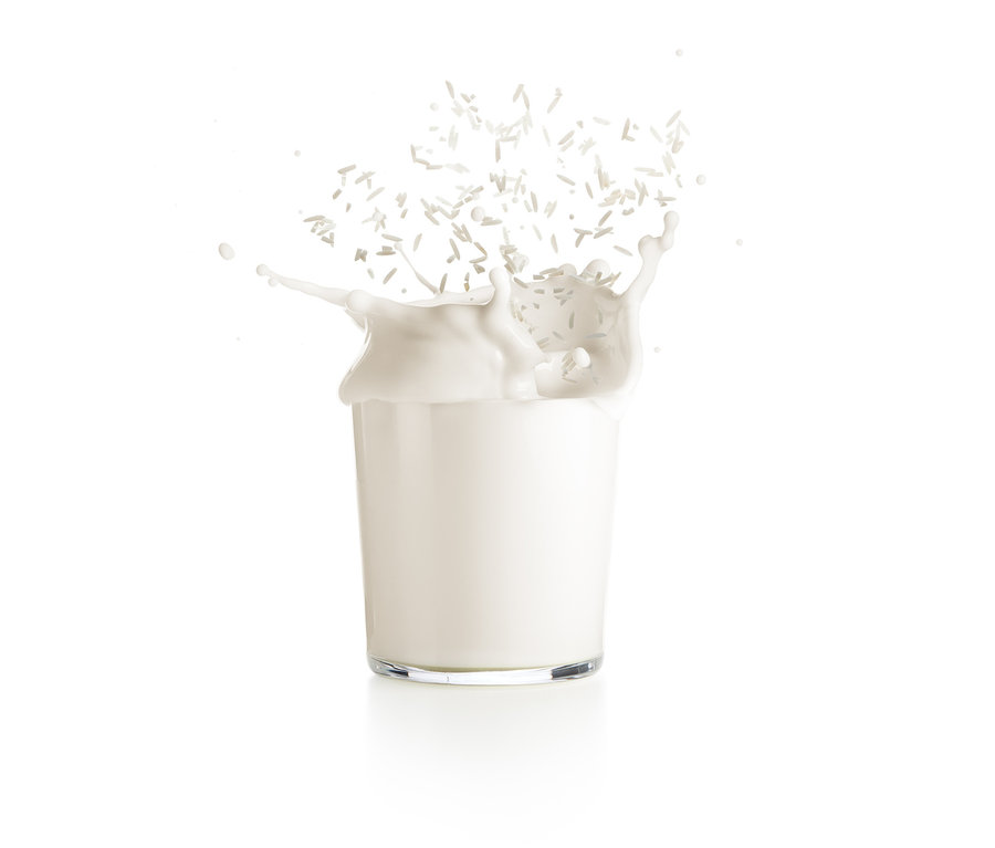 Milch spritzt aus einem transparenten Glas, während Kokosnussstücke um sie herum schweben. Lékué-Nuss-und-Getreidemilch-Maker ist möglicherweise im Einsatz.