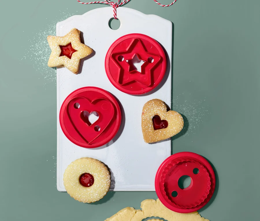 Linzer-Plätzchen-Ausstecher (3 Stk.) auf einem weißen Brett mit Stern-, Herz- und Kreisform. Ausgestochene Formen mit Marmelade und Teig.