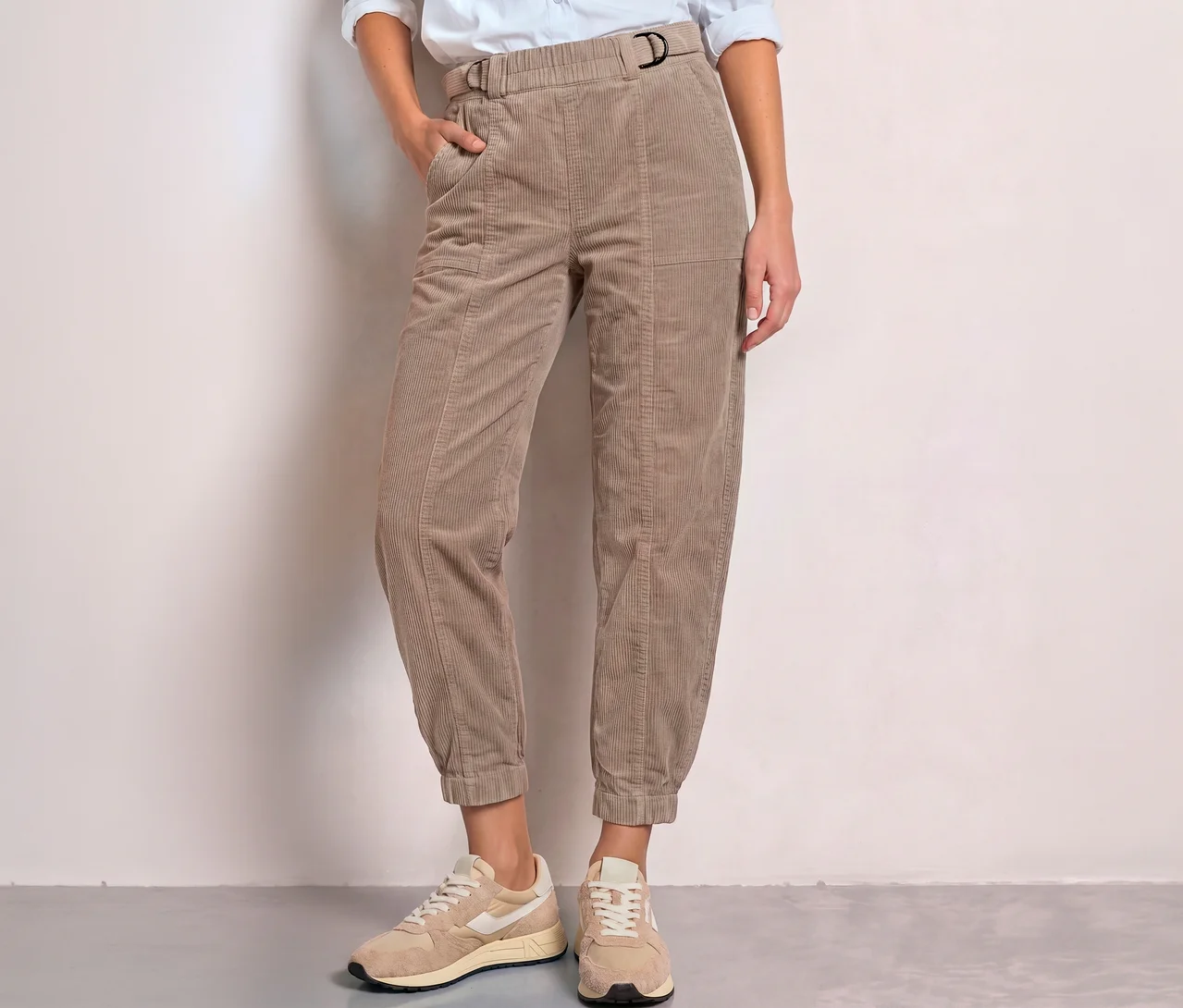 Person trägt beigefarbene Street One Cordhose mit D-Ring-Schnalle und Gummibund, eine Hand in der Tasche, dazu helle Sneaker.