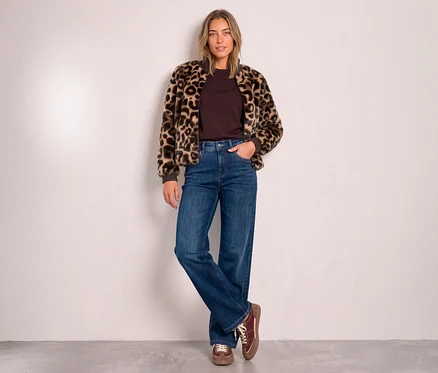 Eine Frau steht mit einer Hand in der Tasche und gekreuzten Beinen, trägt einen Street One Blouson mit Leopardenmuster über einem dunkelbraunen Oberteil, blaue weite Jeans und braune Schnürschuhe.
