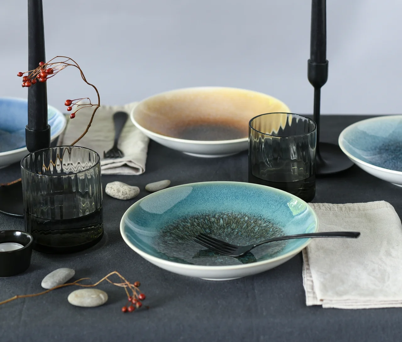 Ein gedeckter Tisch mit Schalen des creaTable Bowl-Sets »Caldera«, dunklen Gläsern, Besteck, Servietten, schwarzen Kerzenständern und roten Beeren.