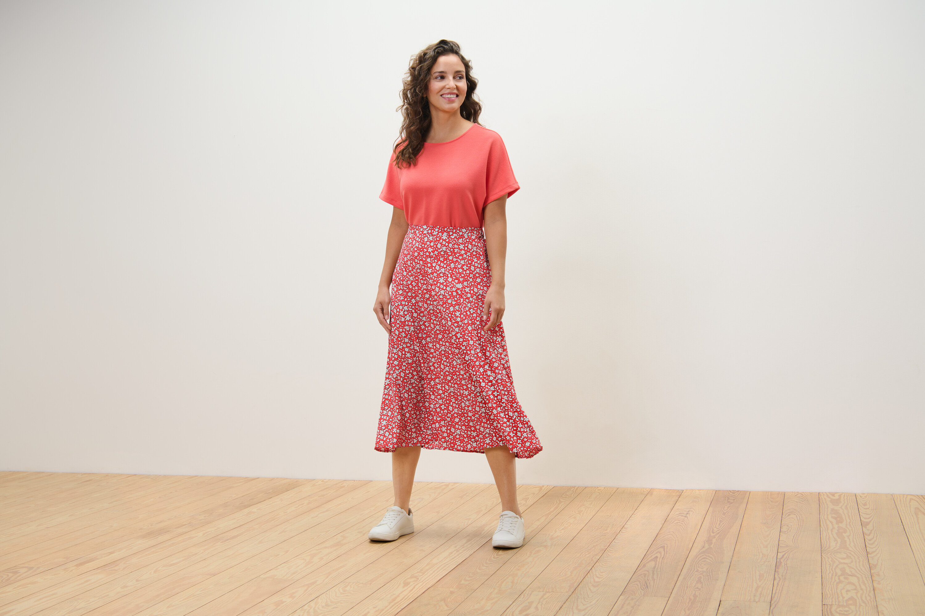 Eine Frau steht auf einem Holzboden und trägt einen korallfarbenen, bedruckten Midirock.