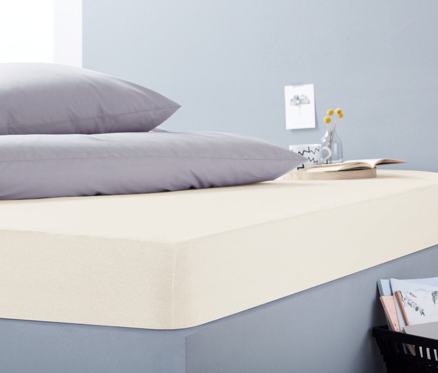 Zwei graue Kissen liegen auf einem beigen Jersey-Spannbettlaken in Übergröße auf einem Bett.