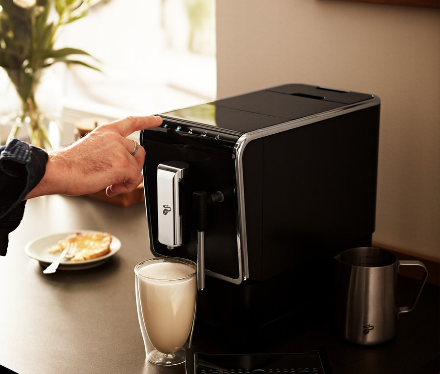 Mann drückt mit dem Finger auf einen Knopf des anthrazitfarbenen »Esperto Latte« Tchibo Kaffeevollautomaten.