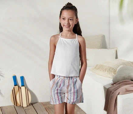 Mädchen trägt ein weisses 2 Tops aus Bio-Baumwolle und gestreifte Shorts.