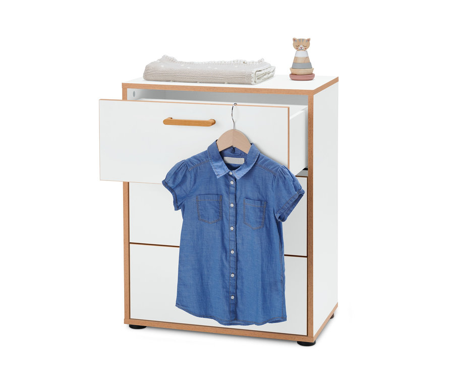 Eine weiße Kommode mit Furnierkante, auf der ein gefalteter Pullover und ein Holzspielzeug liegen. An der offenen oberen Schublade hängt ein blaues Jeanskleid an einem Kleiderbügel.