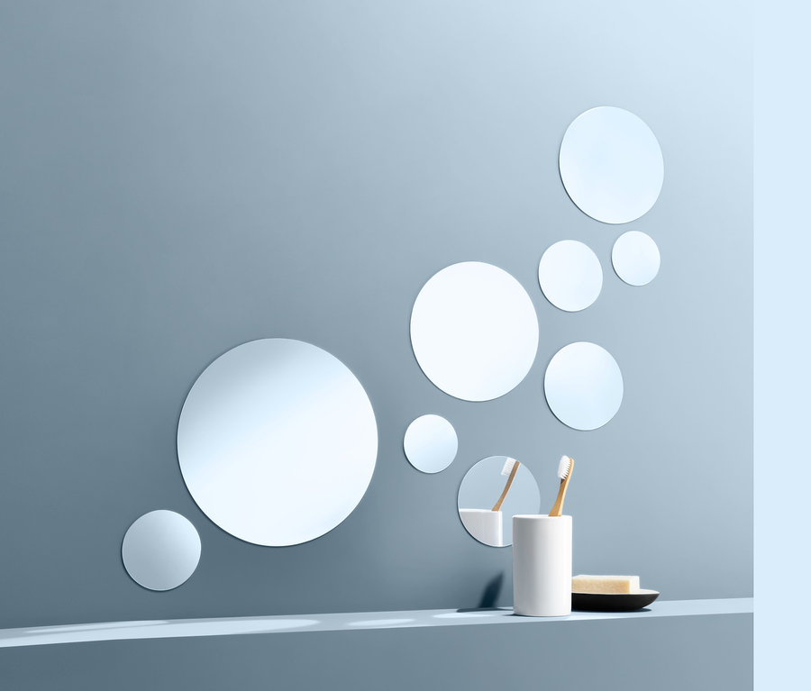 Neun selbstklebende Spiegelsticker sind an einer blauen Wand angebracht. Auf einem Regal stehen ein Becher mit zwei Zahnbürsten und Seife auf einem Teller.