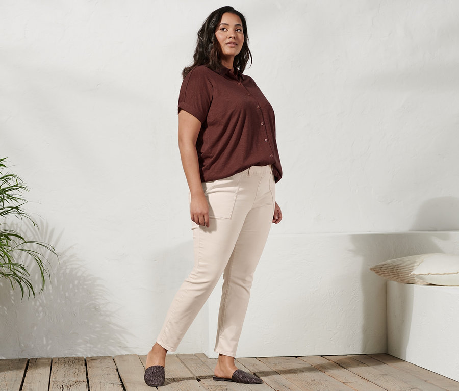 Frau posiert in Mules, Treggings und Blusenshirt mit Knopfleiste.