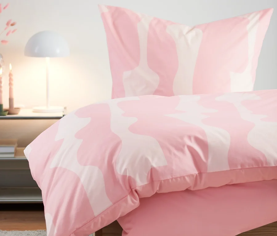 Rosa Premium-Baumwoll-Bettwäsche auf einem Bett neben einem Tisch mit Lampe und Vase.