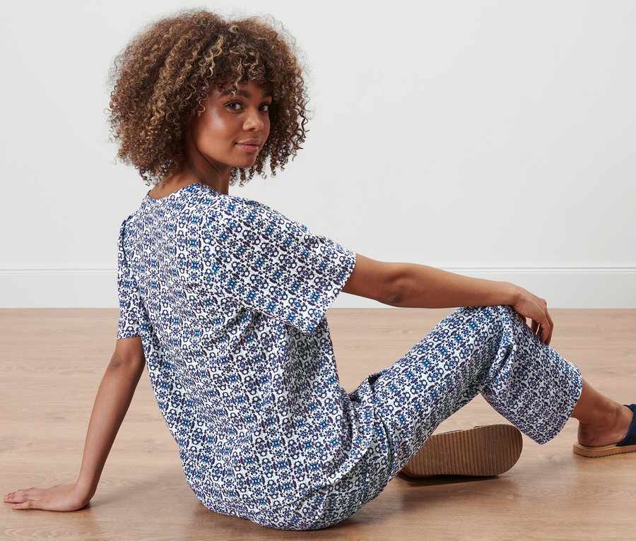 Frau sitzt auf dem Boden und trägt eine Bluse mit Alloverprint und eine Hose.