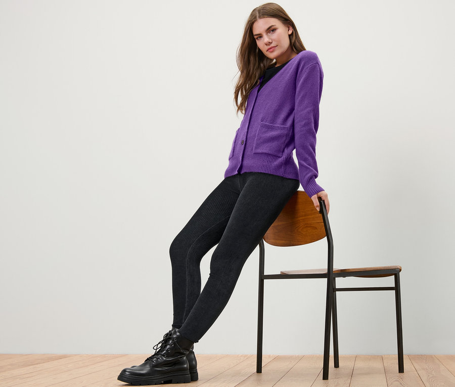 Frau sitzt auf einem Stuhl und trägt eine lila Strickjacke mit Wolle.