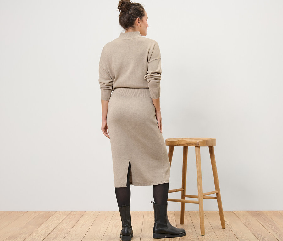 Frau steht mit dem Rücken zur Kamera und trägt einen Strickrock, Strumpfhose und Stiefel.