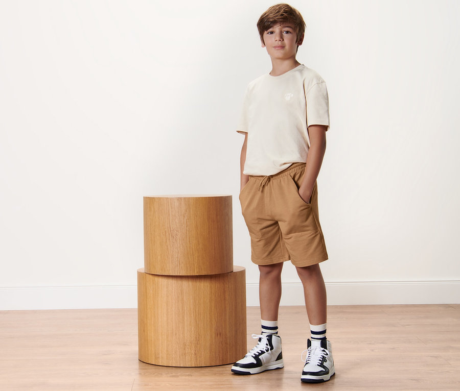 Junge steht neben zwei Kinder-Sweatshorts.