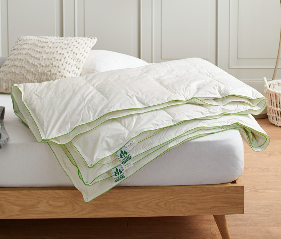 Eine gefaltete irisette® greenline 4-Jahreszeiten-Daunendecke in Normalgröße liegt auf einem Bett.