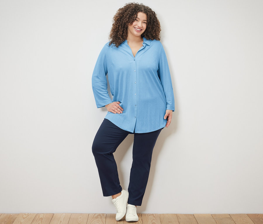 Frau posiert auf Holzboden mit hellblauer Piqué-Jerseybluse und navy Stretchhose.