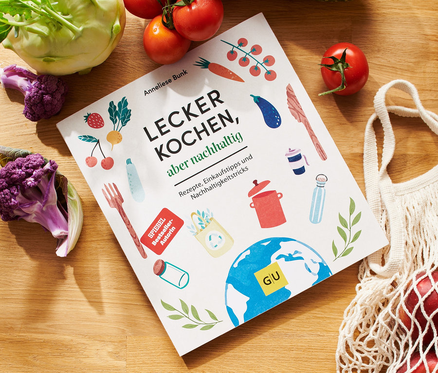 Kochbuch »Lecker kochen, aber nachhaltig« liegt auf Holztisch mit Tomaten, Blumenkohl, Kohlrabi, Äpfeln in Stoffbeutel und Schüsseln.