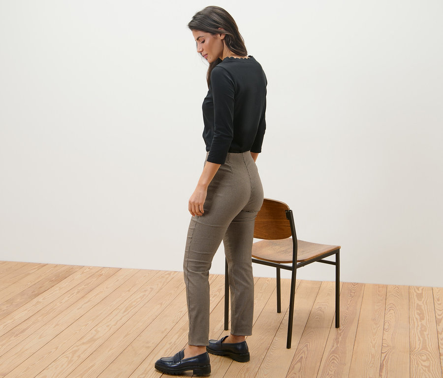 Frau steht seitlich und trägt eine Stretchhose mit Hahnentritt-Jacquard und ein schwarzes Oberteil.