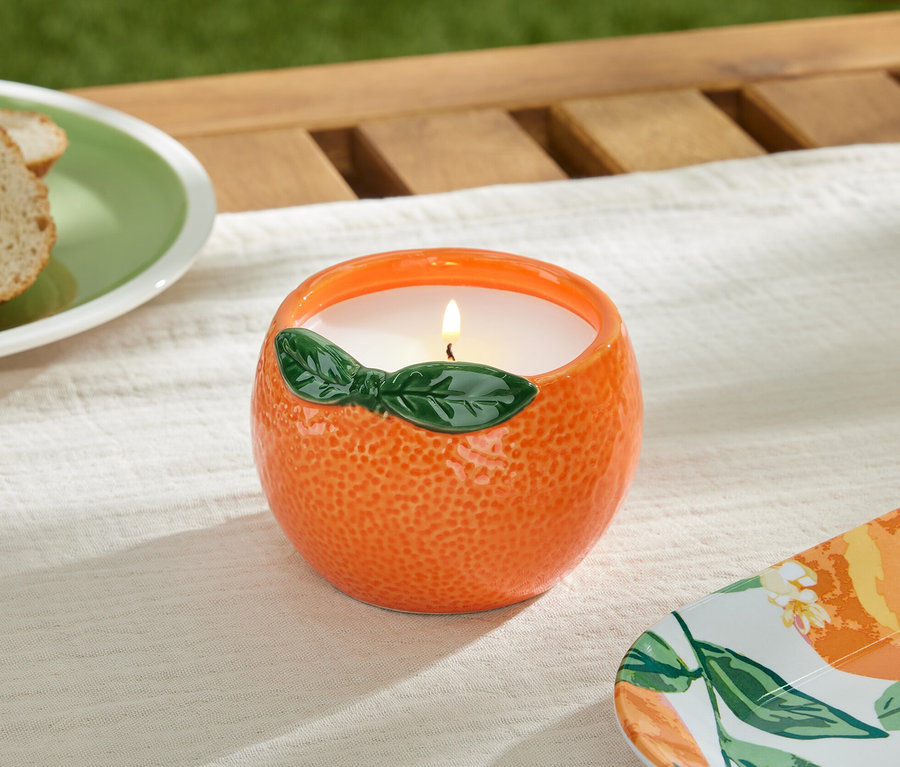 Eine brennende Citronellakerze in einem orangefarbenen Behälter auf einem Tisch.