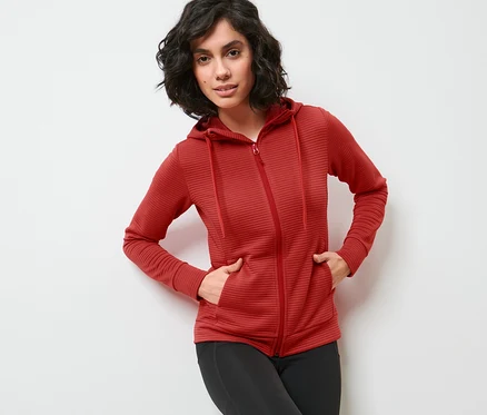Frau posiert in roter Kapuzenjacke und schwarzen Leggings.