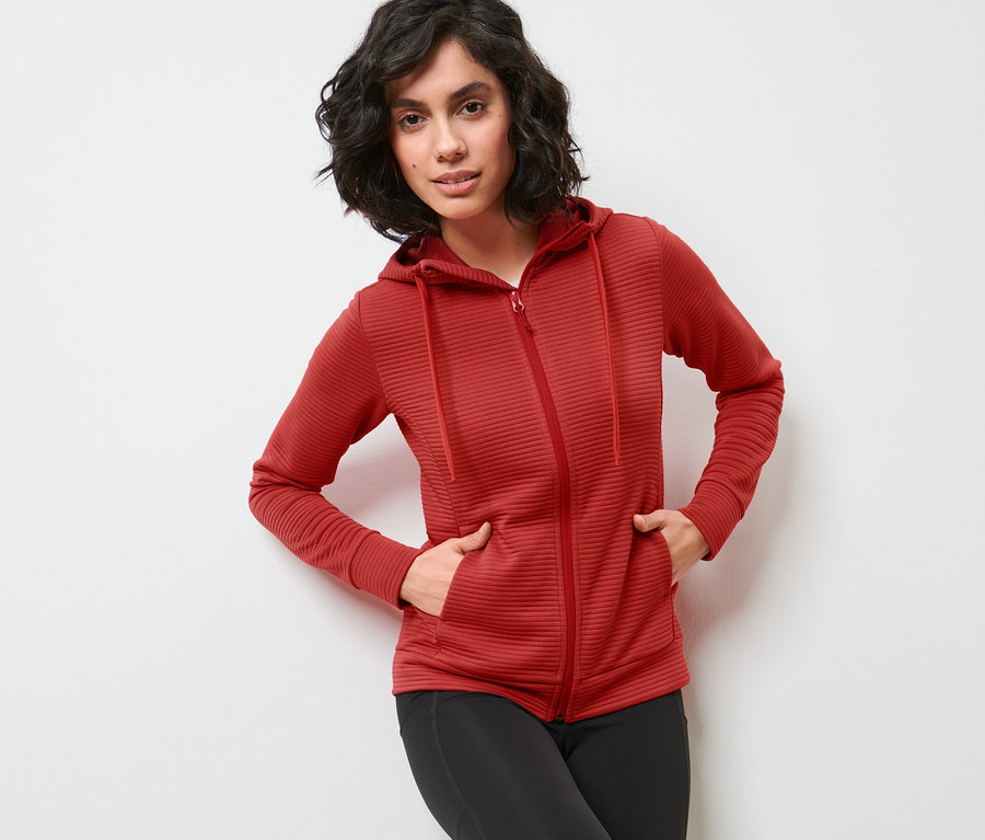 Frau posiert in roter Kapuzenjacke und schwarzen Leggings.