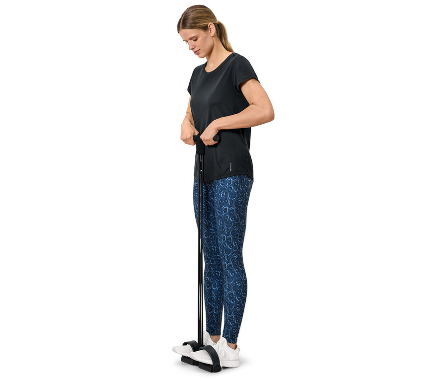 Frau trainiert mit einem Fitnessgerät, sie trägt ein schwarzes T-Shirt und blaue Leggings.