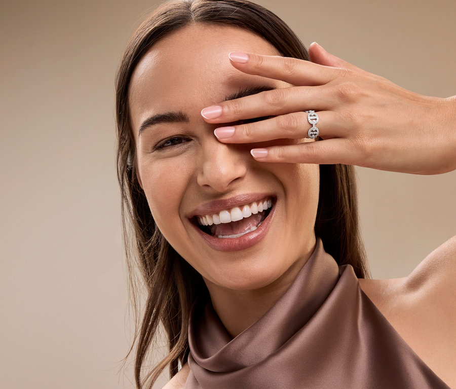 Eine lächelnde Frau bedeckt ihr Auge mit der Hand, am Ringfinger trägt sie einen silbernen Ring.