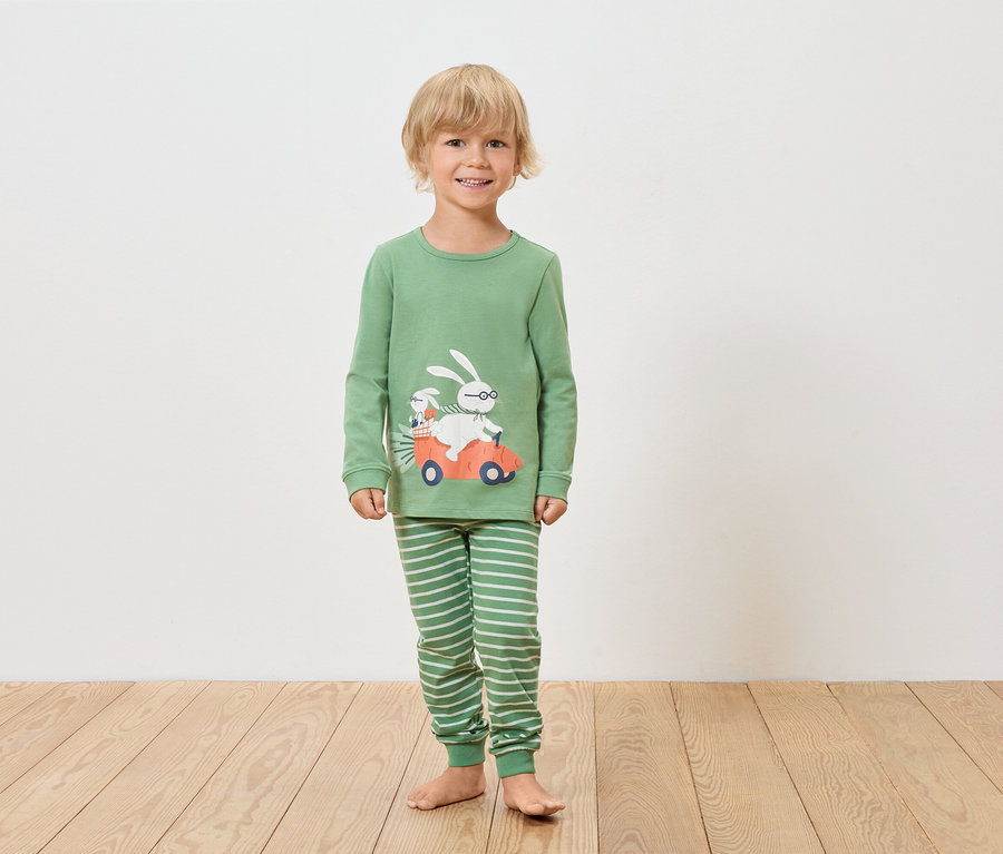 Ein Junge trägt einen grünen langärmligen Pyjama und gestreifte Hosen mit einem Hasenmotiv in einem Auto.