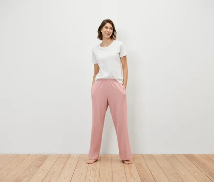 Frau steht mit Händen in den Taschen einer rosafarbenen Jogginghose und trägt ein weißes T-Shirt.