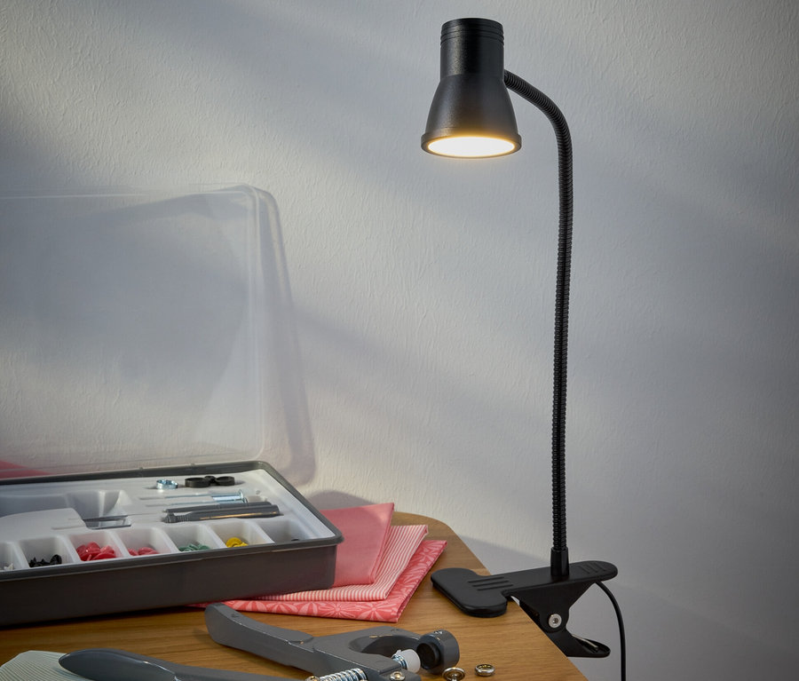 Eine schwarze LED-Klemmleuchte steht auf einem Tisch neben einem Nähzeug.