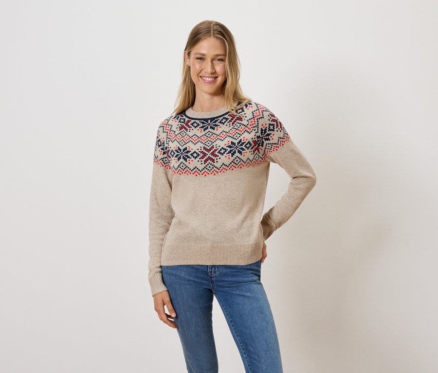 Frau posiert in einem beigen Pullover mit Muster und Jeans.