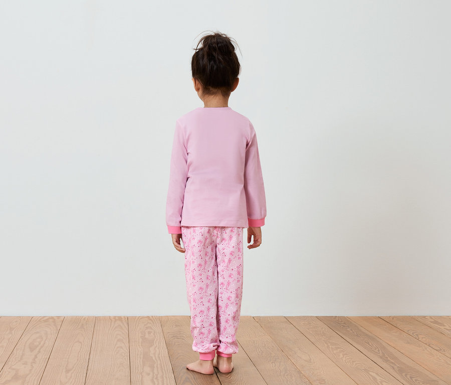 Mädchen im rosa Pyjama steht mit dem Rücken zur Kamera.