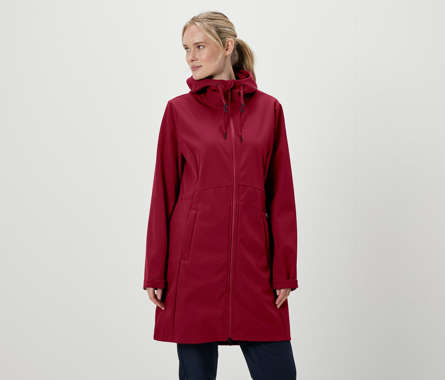 Blonde Frau in weinroter Kapuzenjacke mit Reißverschluss und Hose vor weißem Hintergrund.