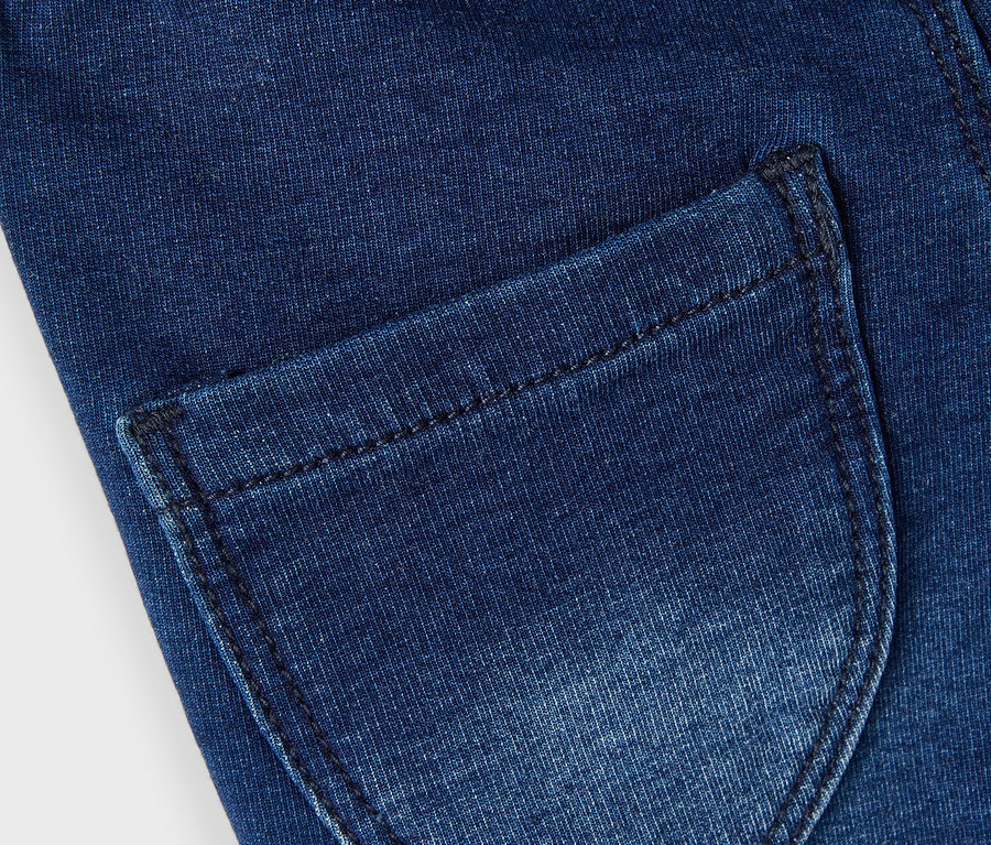 Detailaufnahme einer dunkelblauen Jeans mit einer Gesäßtasche und einem glitzernden Bund.