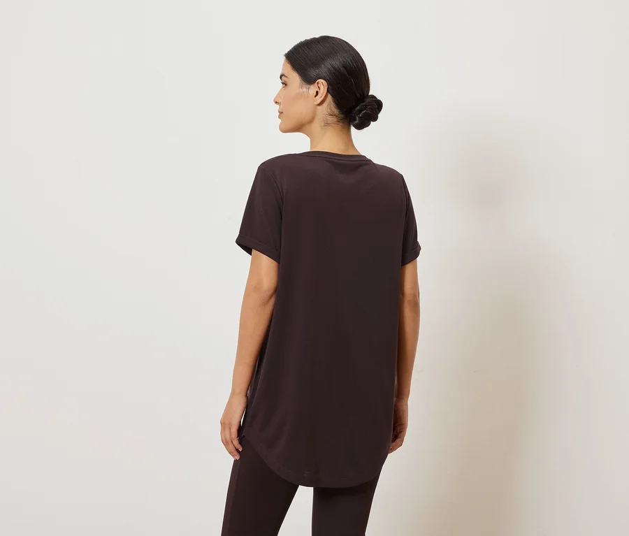 Frau von hinten in braunem T-Shirt und Leggings vor weißem Hintergrund.