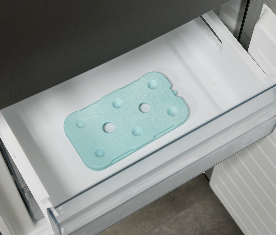 Eine hellblaue Kühlmatte mit kreisförmigen Vertiefungen liegt in einer Schublade im Kühlschrank.