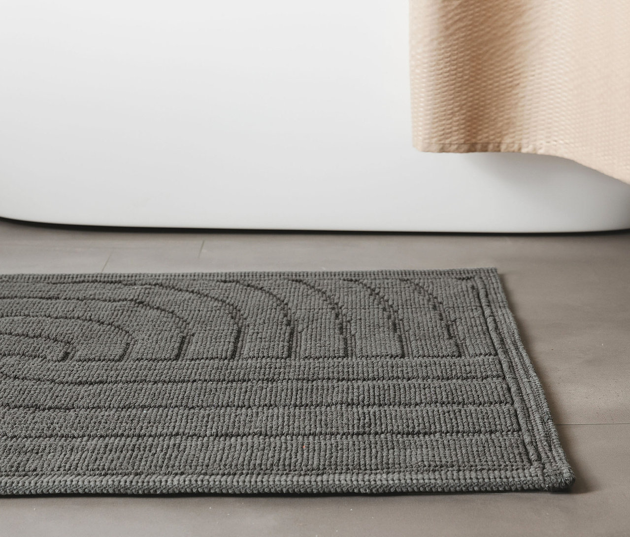 Anthrazitfarbene Badematte »Jojo« von benuta mit Wellenmuster, 50 x 80 cm, liegt vor einer Badewanne.