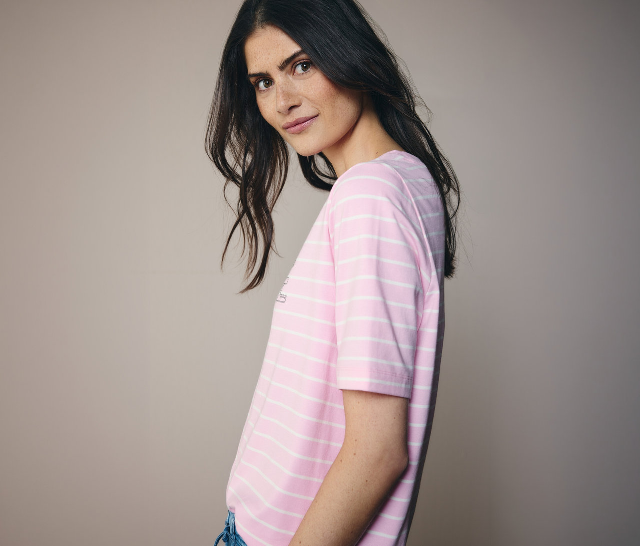 Frau blickt über ihre Schulter und trägt ein rosa-weiß gestreiftes CECIL Shirt.