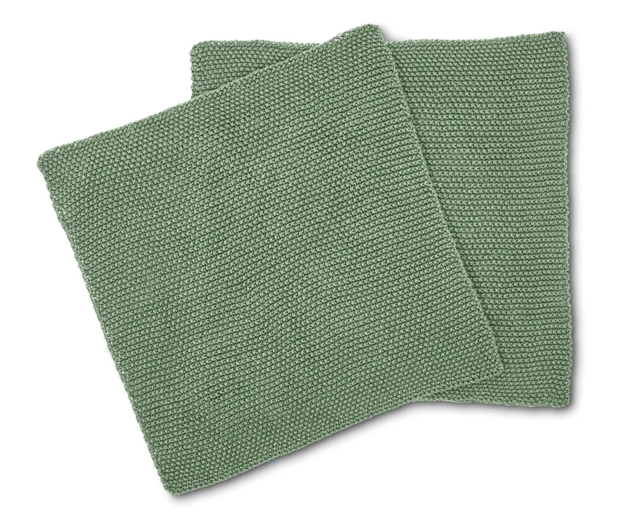 Zwei quadratische, hellgrüne Kissen mit Strickmuster liegen übereinander.