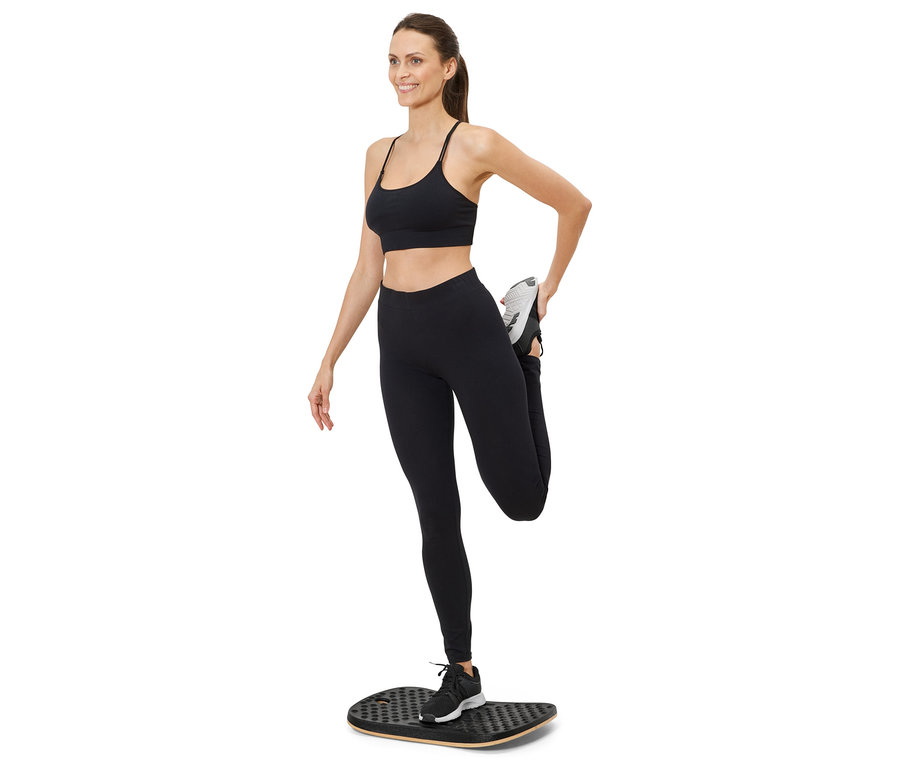 Frau dehnt Bein auf Balance Board, trägt Sportbekleidung.