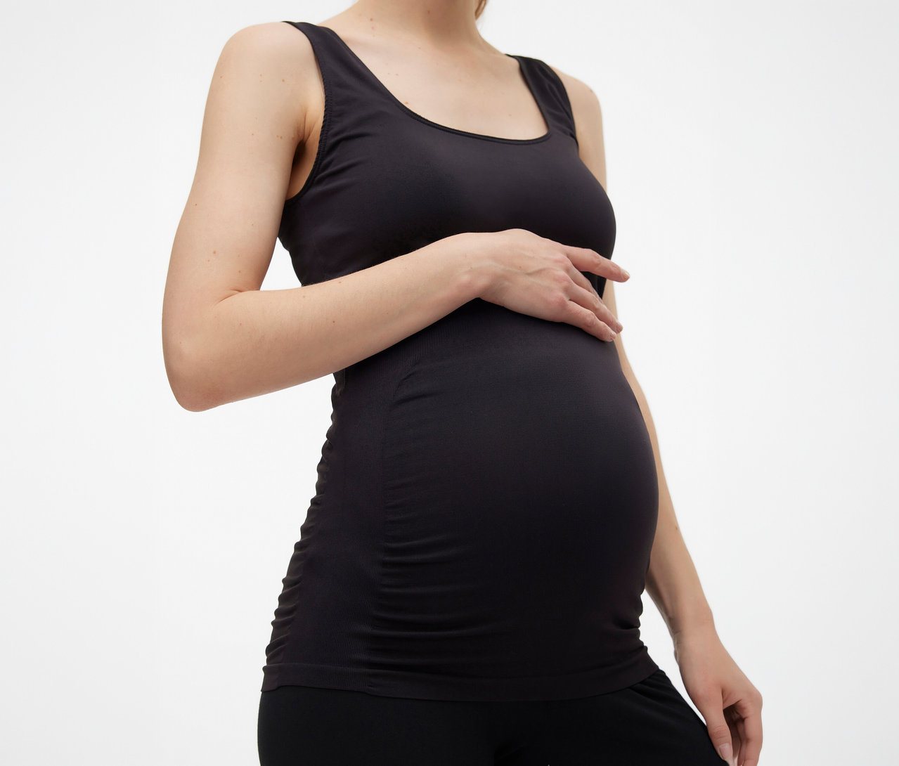 Schwangere Frau mit schwarzem MAMALICIOUS Tanktop »MLHEAL« in Einheitsgröße, die ihre Hand auf ihren Bauch legt.