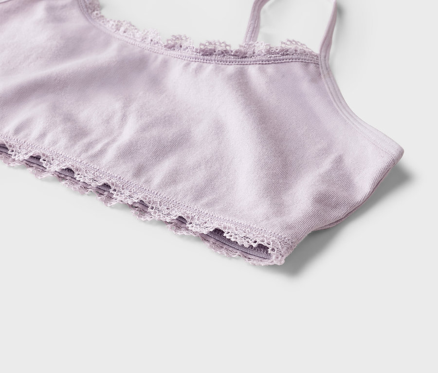Nahaufnahme eines hellvioletten Bralettes mit zarter Spitzenborte am oberen und unteren Rand sowie dünnen Schulterträgern.