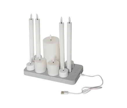 Neun weiße LED-Kerzen unterschiedlicher Größen, darunter Stumpen- und Teelichtkerzen, auf einer grauen Ladestation mit angeschlossenem USB-Kabel.